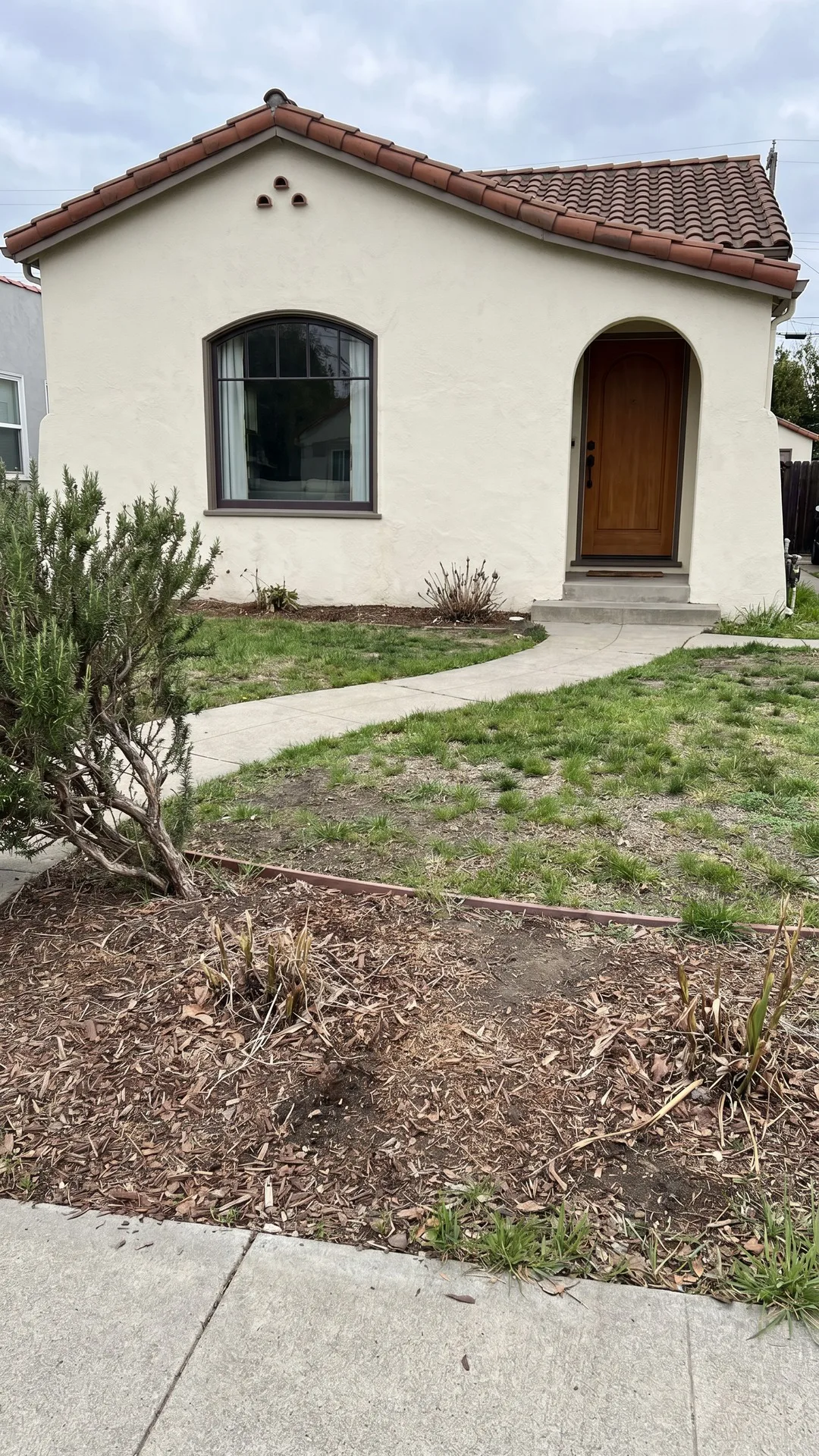 Before photo of a Spanish-style front yard with patchy lawn and bare beds